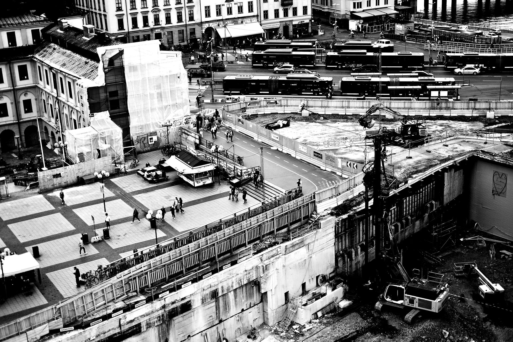An urban construction site at street level, bounded by existing buildings and traffic.