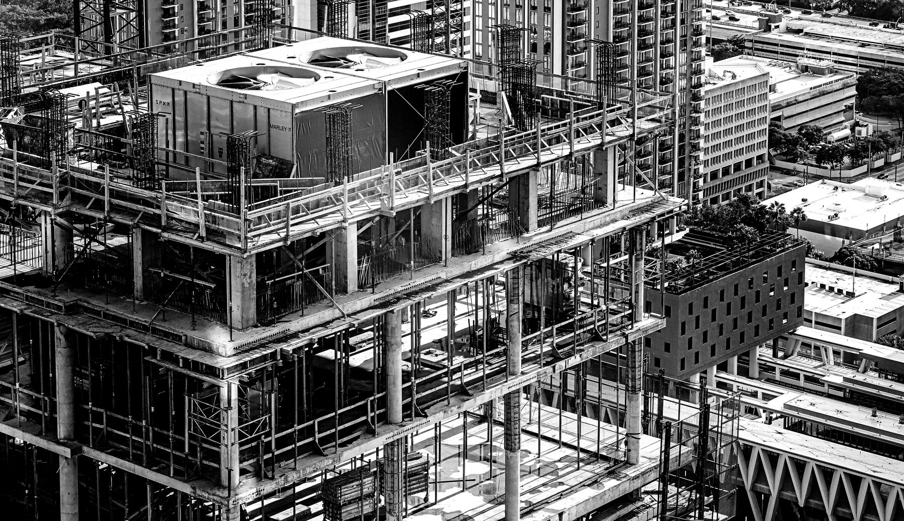 The structural frame of a building under construction, seen from above against the surrounding city.